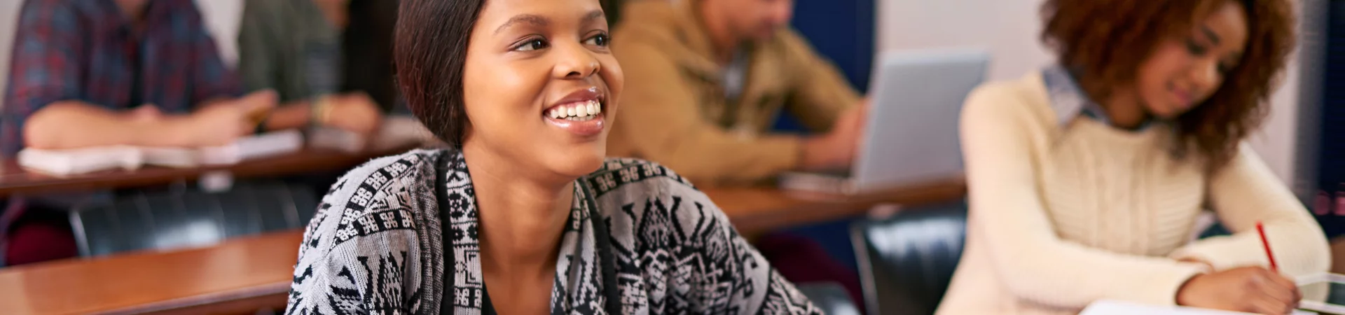 A smiling woman in a classroom surrounded by engaged students, highlighting a positive learning environment.